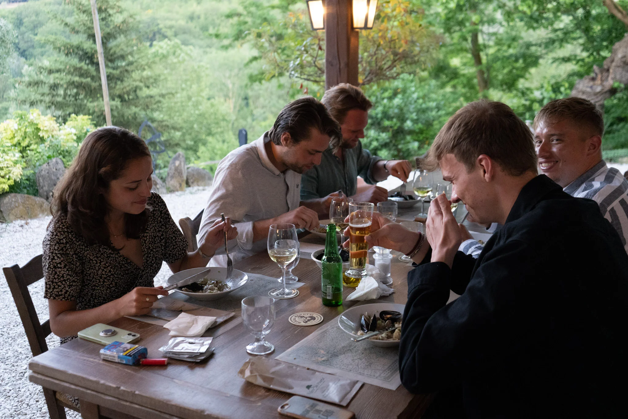 Vrienden aan een lange houten tafel onder het lampenlicht in de tuin